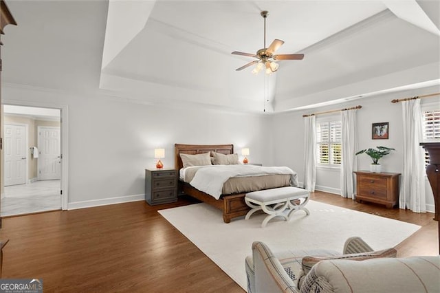 bedroom featuring a ceiling fan, baseboards, a tray ceiling, and wood finished floors