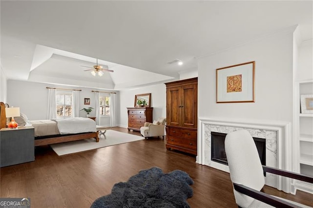 bedroom featuring a premium fireplace, a ceiling fan, vaulted ceiling, a tray ceiling, and dark wood finished floors