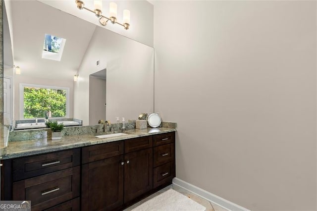 bathroom featuring vaulted ceiling with skylight, vanity, and baseboards