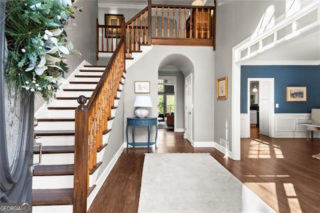 foyer featuring visible vents, ornamental molding, wood finished floors, and a towering ceiling