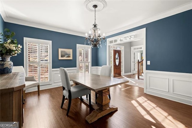 dining room with crown molding, a chandelier, dark wood-type flooring, and wainscoting