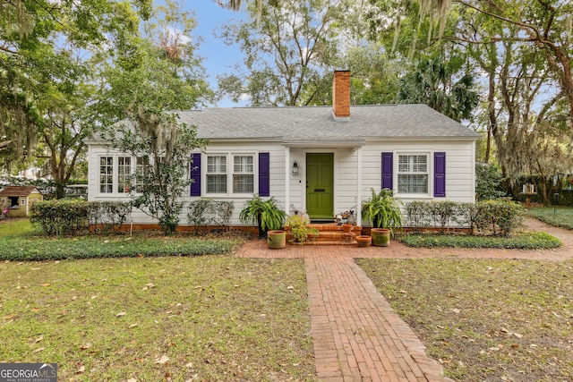 single story home with a chimney, a front lawn, and roof with shingles