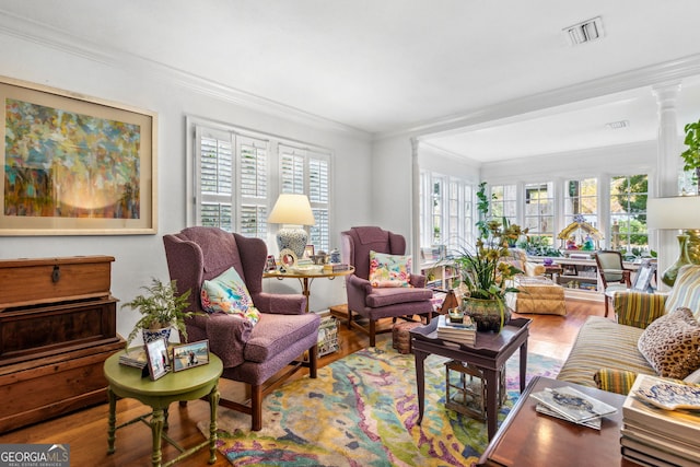 living room with ornate columns, visible vents, wood finished floors, and ornamental molding