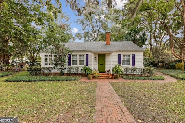 ranch-style home with roof with shingles, a chimney, and a front lawn