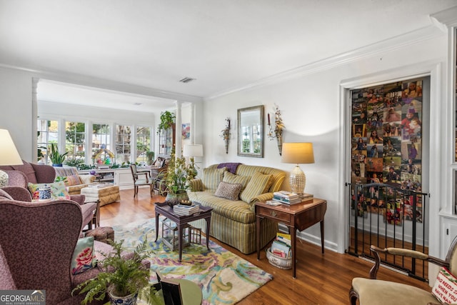 living area featuring visible vents, crown molding, baseboards, and wood finished floors