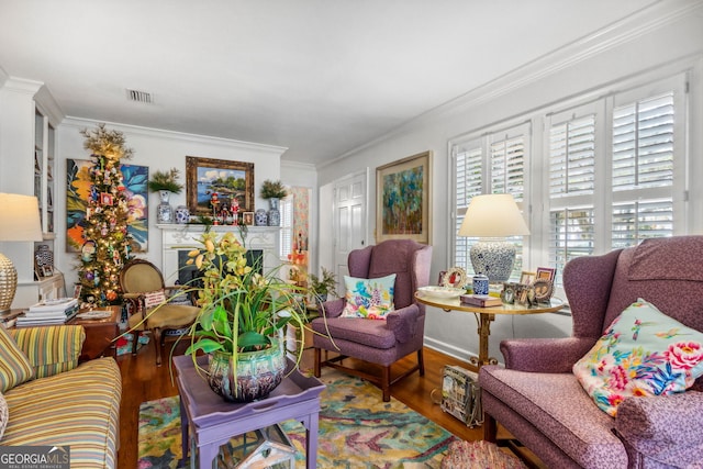 living area with ornamental molding, a fireplace, wood finished floors, and visible vents