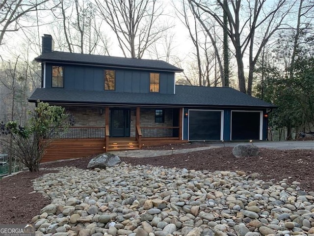 view of front of home featuring a garage, driveway, a chimney, covered porch, and board and batten siding