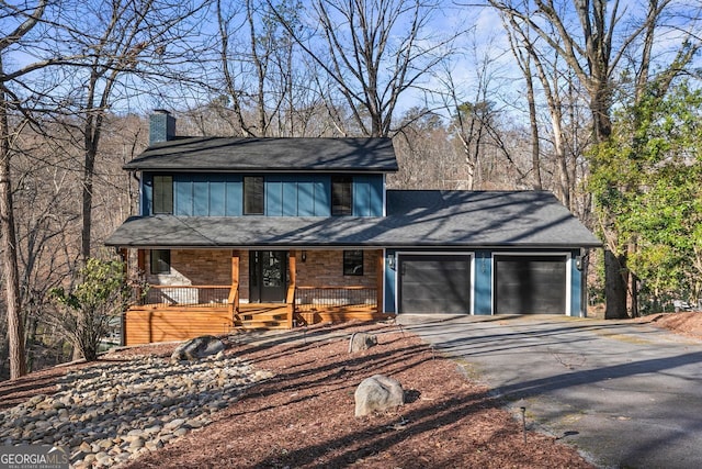 chalet / cabin with covered porch, driveway, a chimney, and an attached garage