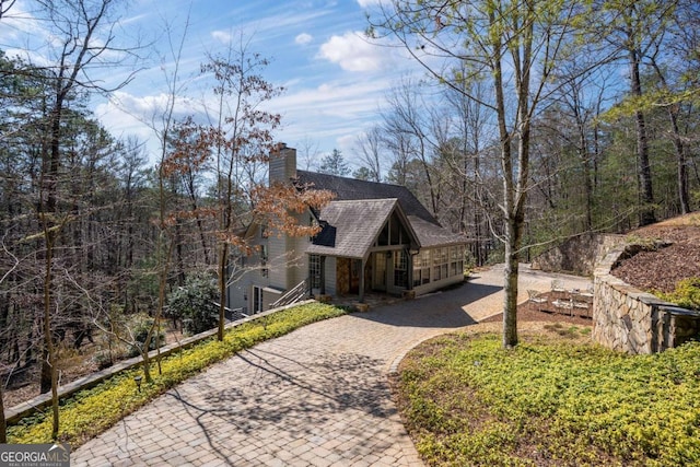 view of property exterior with a shingled roof, a chimney, and decorative driveway