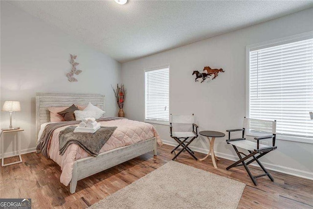 bedroom featuring lofted ceiling, a textured ceiling, wood finished floors, and baseboards