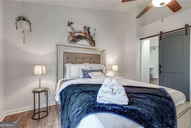 bedroom featuring ceiling fan, a barn door, wood finished floors, and baseboards