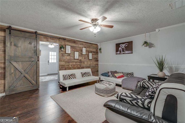 living area featuring ceiling fan, a textured ceiling, a barn door, hardwood / wood-style flooring, and ornamental molding