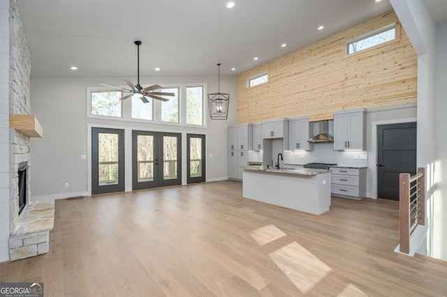 kitchen featuring light wood-style floors, open floor plan, wall chimney range hood, and a stone fireplace