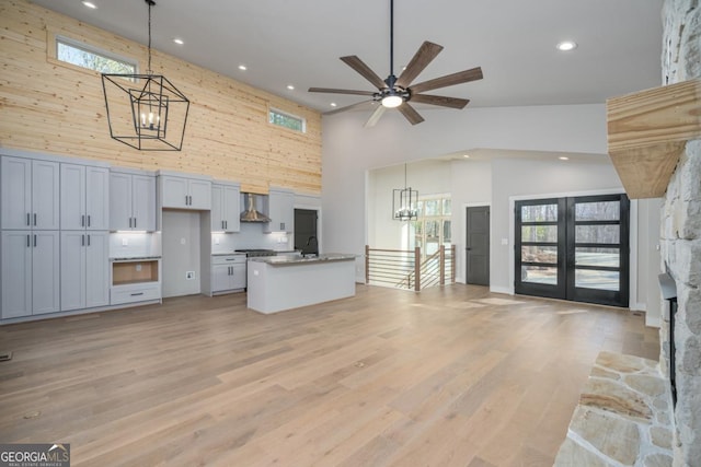 kitchen featuring open floor plan, a high ceiling, light wood-type flooring, wall chimney range hood, and pendant lighting