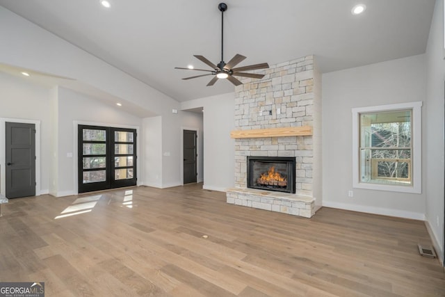 unfurnished living room with light wood finished floors, lofted ceiling, a stone fireplace, french doors, and recessed lighting