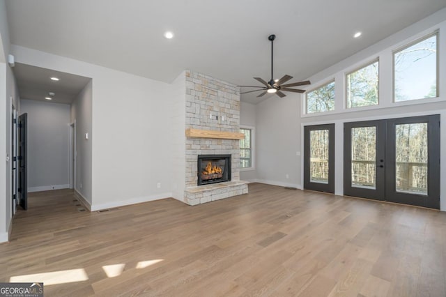 unfurnished living room with high vaulted ceiling, a stone fireplace, recessed lighting, baseboards, and light wood-type flooring