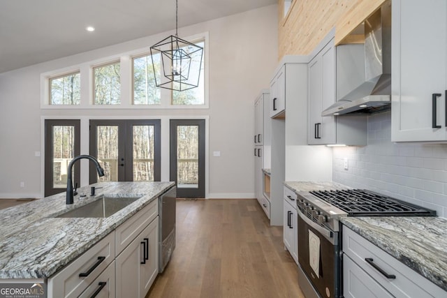 kitchen with wall chimney exhaust hood, wood finished floors, light stone countertops, stainless steel appliances, and a sink