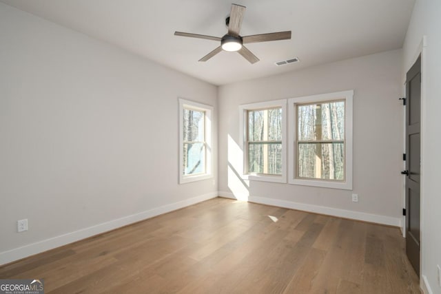 unfurnished room with ceiling fan, wood finished floors, visible vents, and baseboards