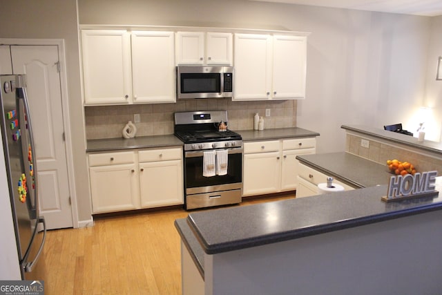 kitchen with stainless steel appliances, dark countertops, light wood-style flooring, and decorative backsplash