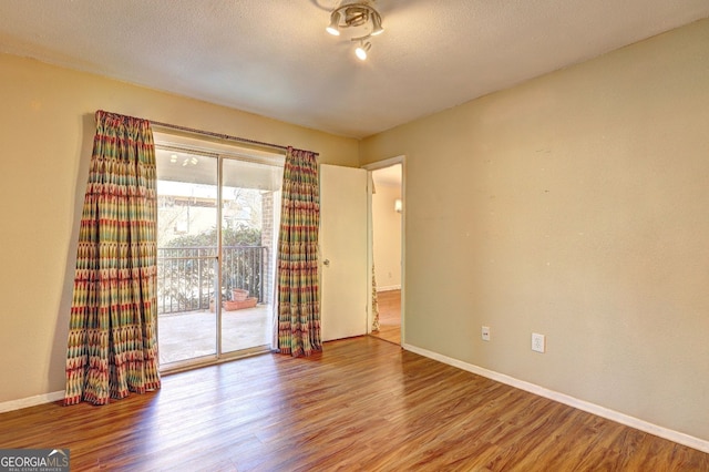 unfurnished room featuring a textured ceiling, baseboards, and wood finished floors