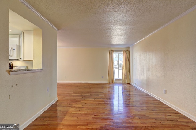 spare room with a textured ceiling, a textured wall, wood finished floors, baseboards, and ornamental molding