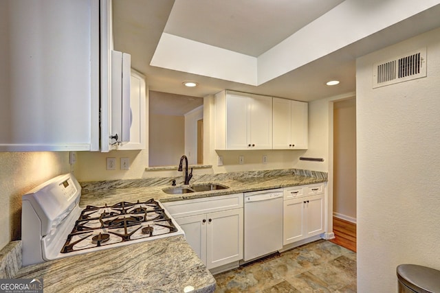 kitchen with light stone counters, visible vents, white cabinets, a sink, and white appliances