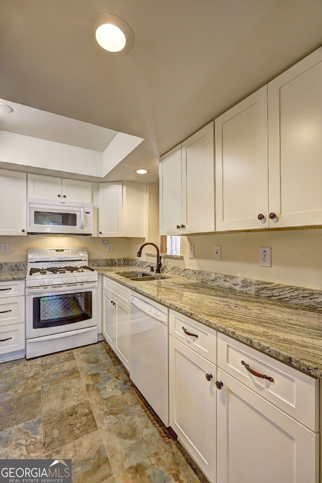 kitchen featuring white appliances, white cabinets, light stone counters, a sink, and recessed lighting