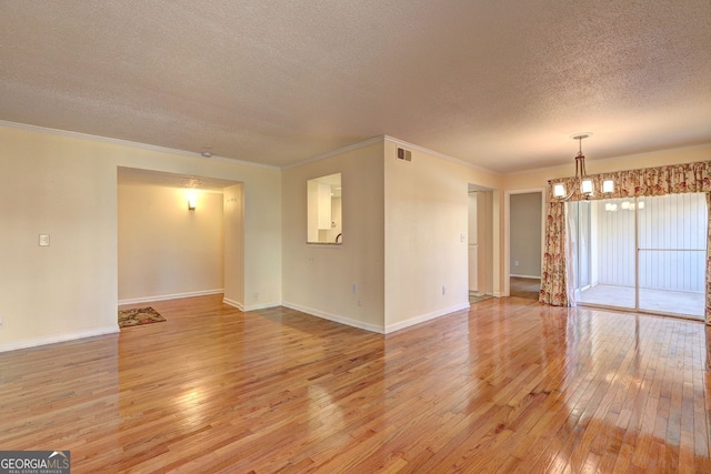 empty room with visible vents, baseboards, light wood-style flooring, an inviting chandelier, and a textured ceiling