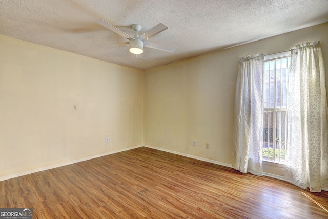 spare room with ceiling fan, a textured ceiling, baseboards, and wood finished floors