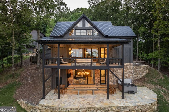 rear view of house with a deck, metal roof, a patio, stone siding, and board and batten siding