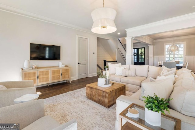 living area with dark wood-style floors, an inviting chandelier, ornamental molding, wainscoting, and stairs