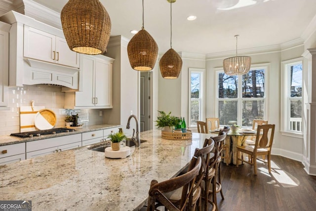 kitchen with a sink, stainless steel gas stovetop, backsplash, dark wood-style floors, and crown molding