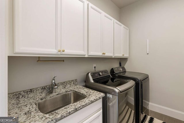 washroom with washer and dryer, cabinet space, a sink, and baseboards