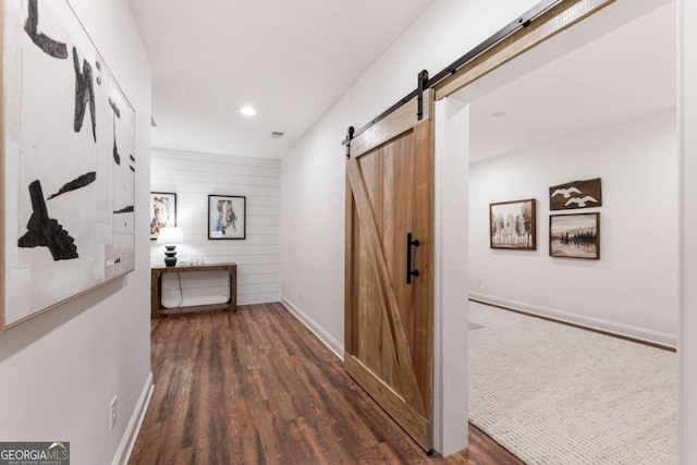 corridor featuring wooden walls, a barn door, wood finished floors, and baseboards