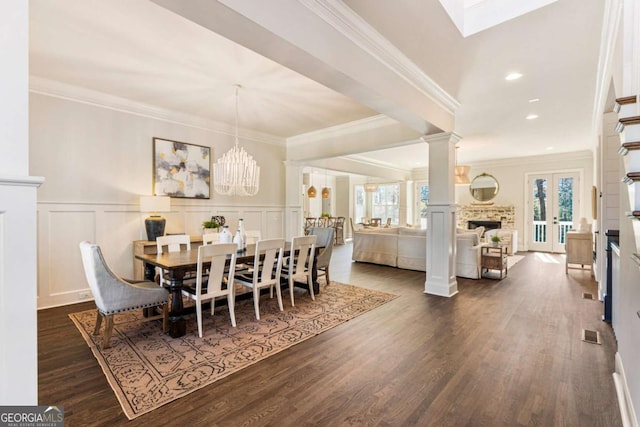 dining space featuring a wainscoted wall, crown molding, dark wood finished floors, decorative columns, and a decorative wall