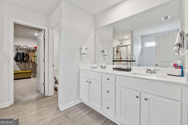 bathroom featuring a sink, double vanity, visible vents, and wood finished floors