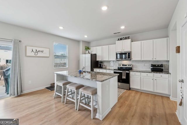 kitchen with a center island with sink, white cabinets, appliances with stainless steel finishes, a breakfast bar, and backsplash