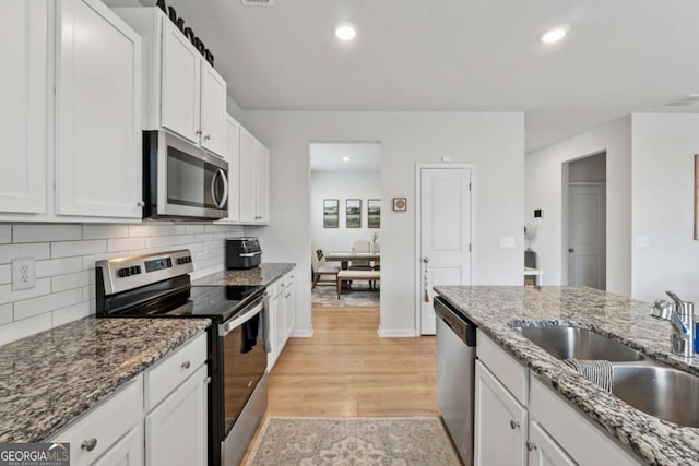 kitchen with appliances with stainless steel finishes, light wood-style floors, white cabinetry, and a sink