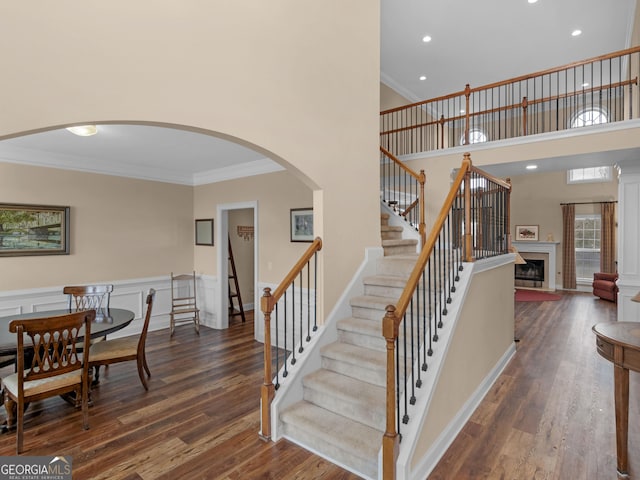 stairway with a fireplace with raised hearth, wood finished floors, and ornamental molding