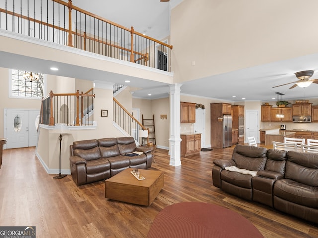 living area featuring stairs, a high ceiling, wood finished floors, and ornate columns