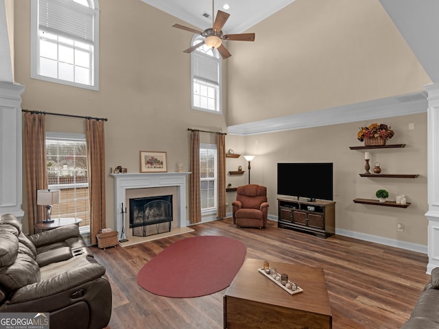 living area featuring decorative columns, a fireplace with flush hearth, baseboards, and wood finished floors