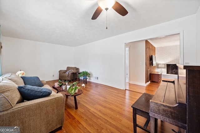 living area with a fireplace, visible vents, a ceiling fan, wood finished floors, and baseboards