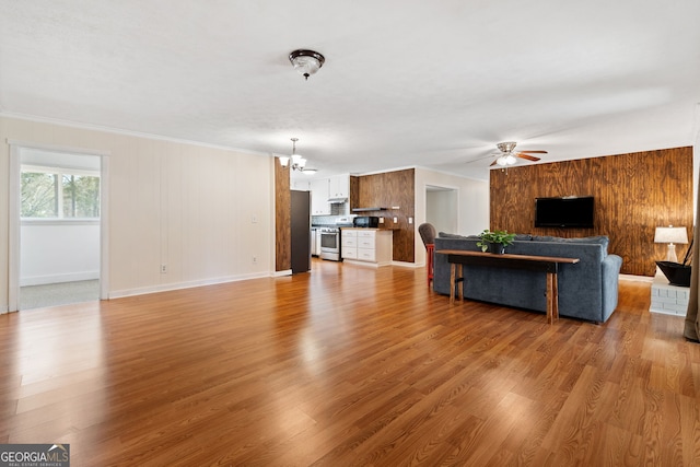 living area with light wood-style floors, wooden walls, baseboards, and ceiling fan with notable chandelier