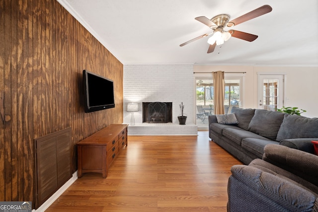 living room featuring a fireplace, visible vents, ornamental molding, wooden walls, and wood finished floors