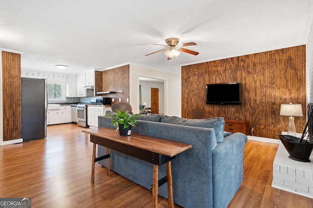 living area featuring a ceiling fan, light wood-style flooring, and crown molding