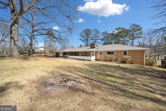 back of property with a sunroom, brick siding, a yard, and a chimney