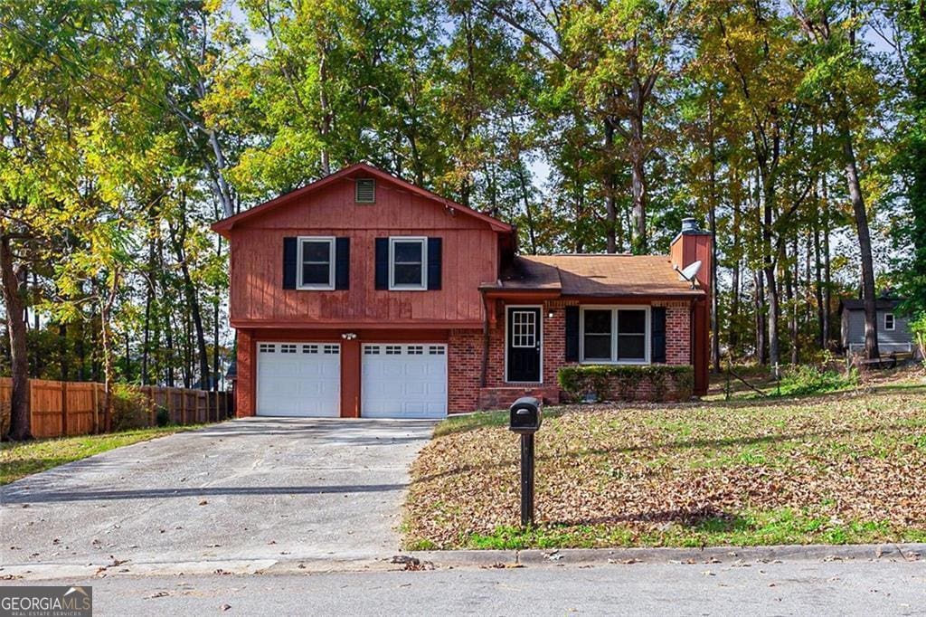 tri-level home with an attached garage, brick siding, fence, driveway, and a chimney