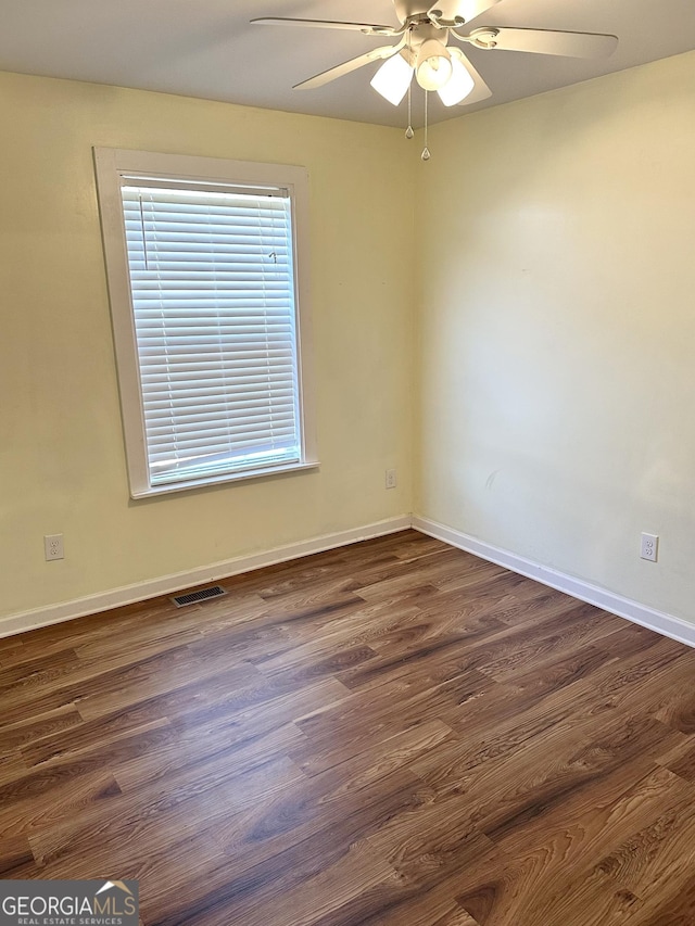 empty room with ceiling fan, dark wood finished floors, visible vents, and baseboards