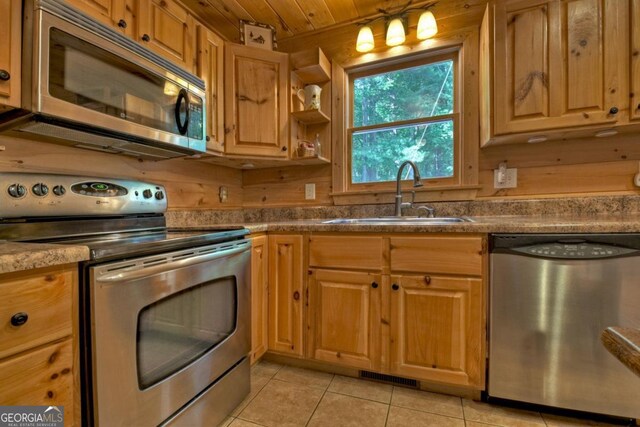 kitchen featuring appliances with stainless steel finishes, light tile patterned flooring, a sink, and wooden walls