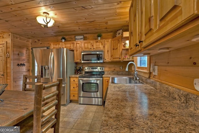 kitchen featuring light tile patterned floors, stainless steel appliances, wood ceiling, a sink, and wood walls